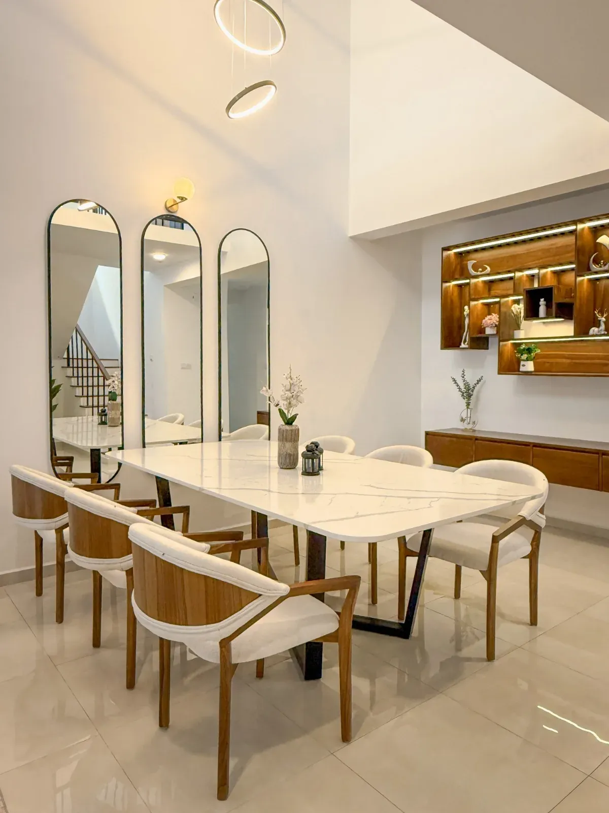 Marble dining table with curved timber-and-cream chairs, arched mirrors and lit shelving beyond