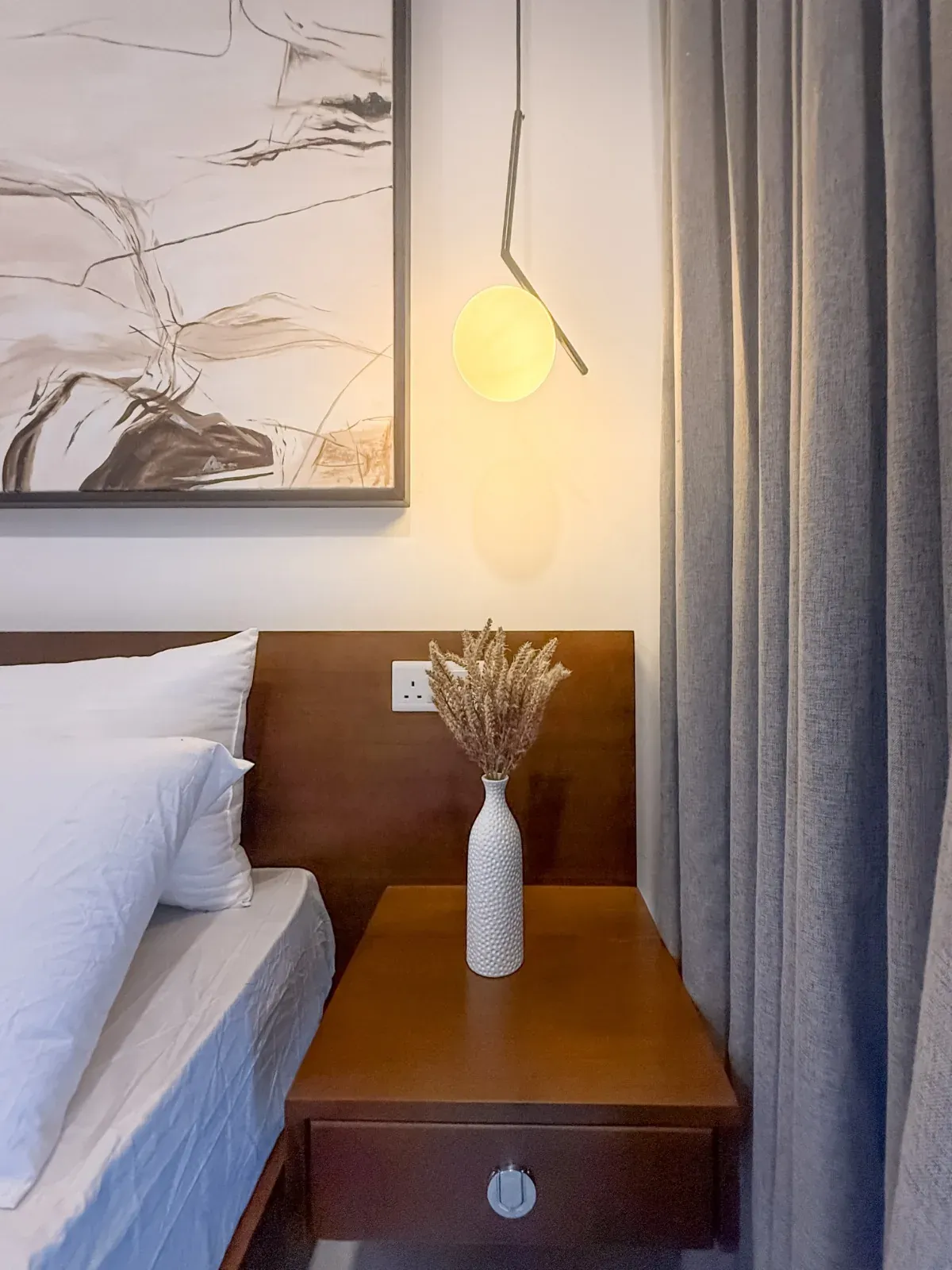 Walnut bedside table with a globe pendant light and a vase of dried stems