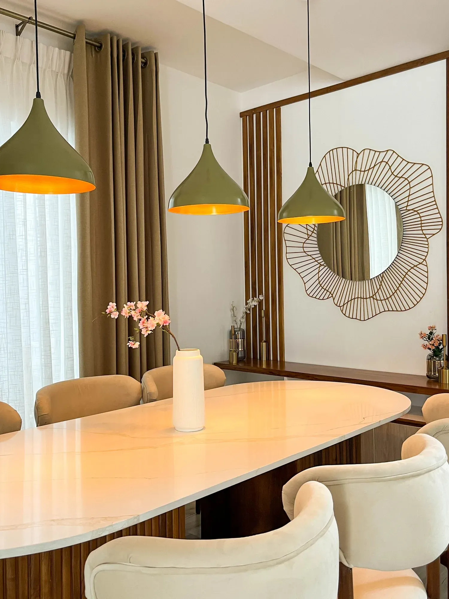 Dining table beside a wall of timber slats framing a sculptural round mirror